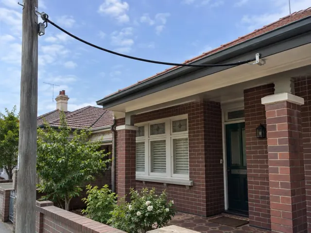 Overhead service cable and point-of-attachment bracket on a brick house exterior in Ryde