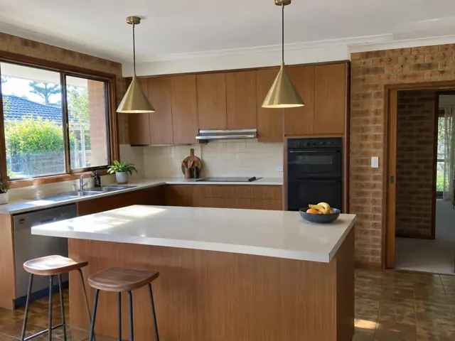 Kitchen with two brass pendant lights over a white island, wood cabinets and brick walls in Putney